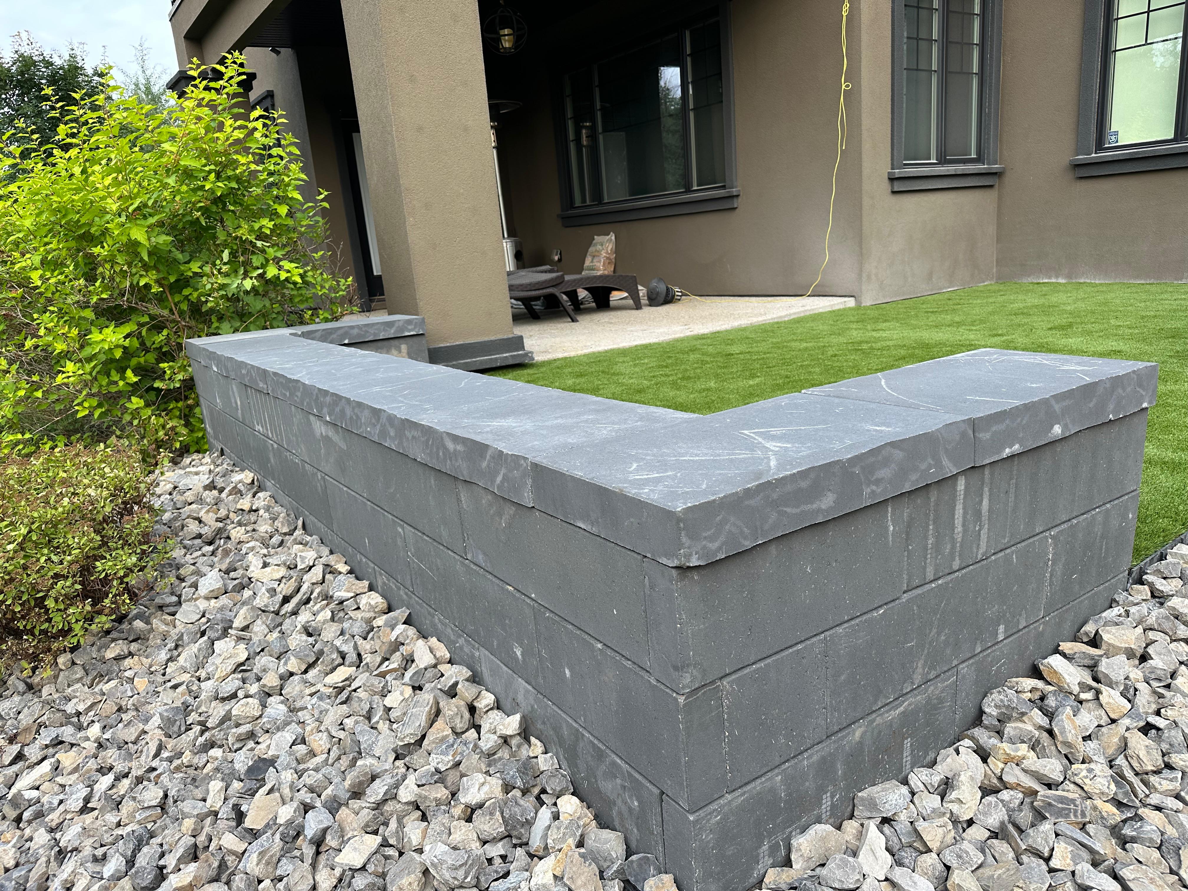 Dark stone retaining wall with cap stones beside artificial turf area on Edmonton property